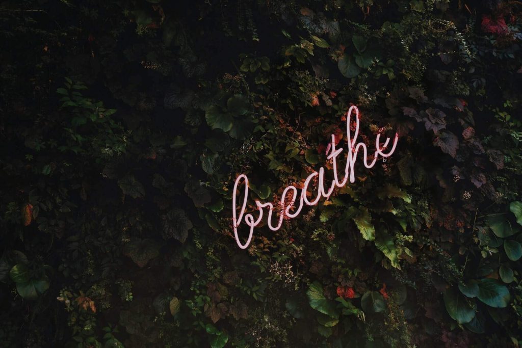 Moving Minds Hypnotherapy - hypnotherapy for smoking a neon sign spelling out breath on a green wall of foliage.